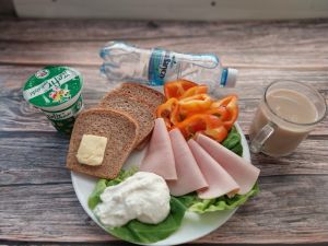 Zdjęcie przedstawia Dietę z ogr.łatwoprzsw. węglowodanów: Chleb Graham  Masło extra  Szynka Drobiowa, parzona, z dodatkiem białka wieprzowego Twarożek  Sałata zielona  Papryka świeża  Kawa zbożowa z mlekiem Kefir Woda źródlana 